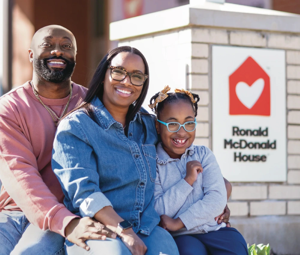 mother father and daughter sitting together by Ronald McDonald house sign