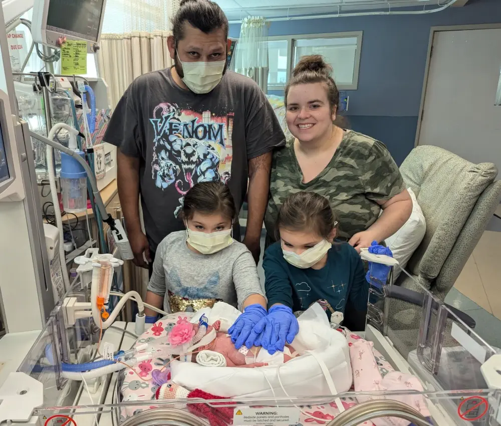 family visiting newborn sibling in hospital room